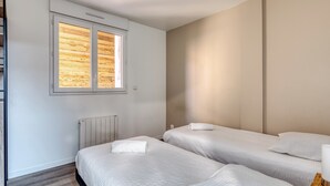 Une chambre avec deux lits, une fenêtre avec des persiennes en bois, un radiateur et un luminaire fixé au mur.