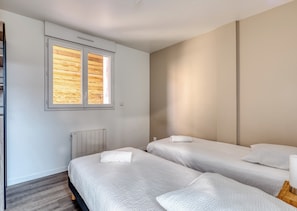 Een slaapkamer met twee bedden, een raam met houten luiken, een radiator en een wandlamp.