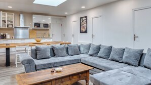 Un salon moderne avec un canapé d’angle gris, une table basse en bois et un coin repas comprenant une table et des chaises en bois.