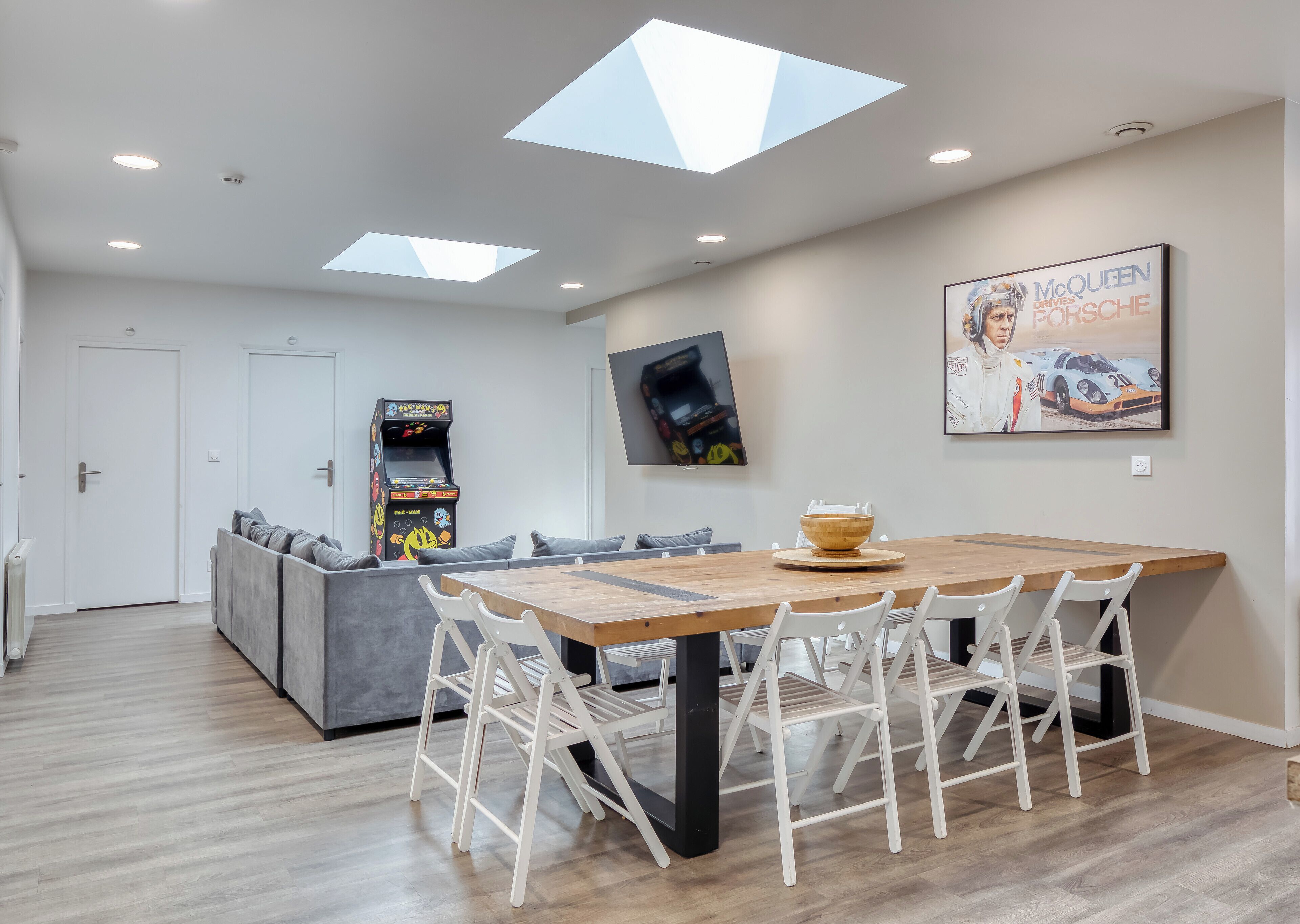 A modern living room with a dining area, a sofa, a gaming console, and a poster on the wall.