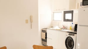 A modern kitchen with a dining area, including a round table with chairs, a washing machine, and a refrigerator.