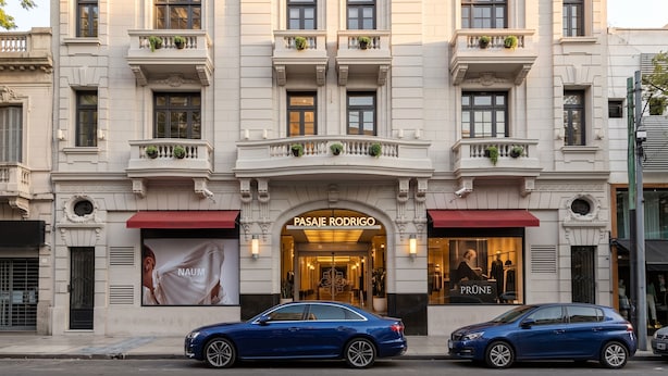 A building with a grand entrance, two visible storefronts, and parked cars.