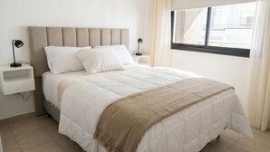 A bed with a beige headboard, white bedding, and a brown throw blanket. There are two bedside tables with lamps.