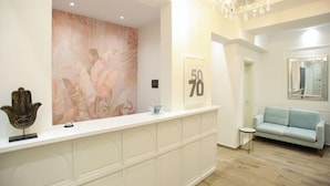 Un espace d’accueil avec un comptoir blanc, une fresque murale à motifs floraux, un panneau avec des chiffres encadré, un canapé bleu clair et un miroir au mur.