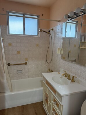 A bathroom with a bathtub, a shower, a sink with gold faucets, a mirror, and a window.