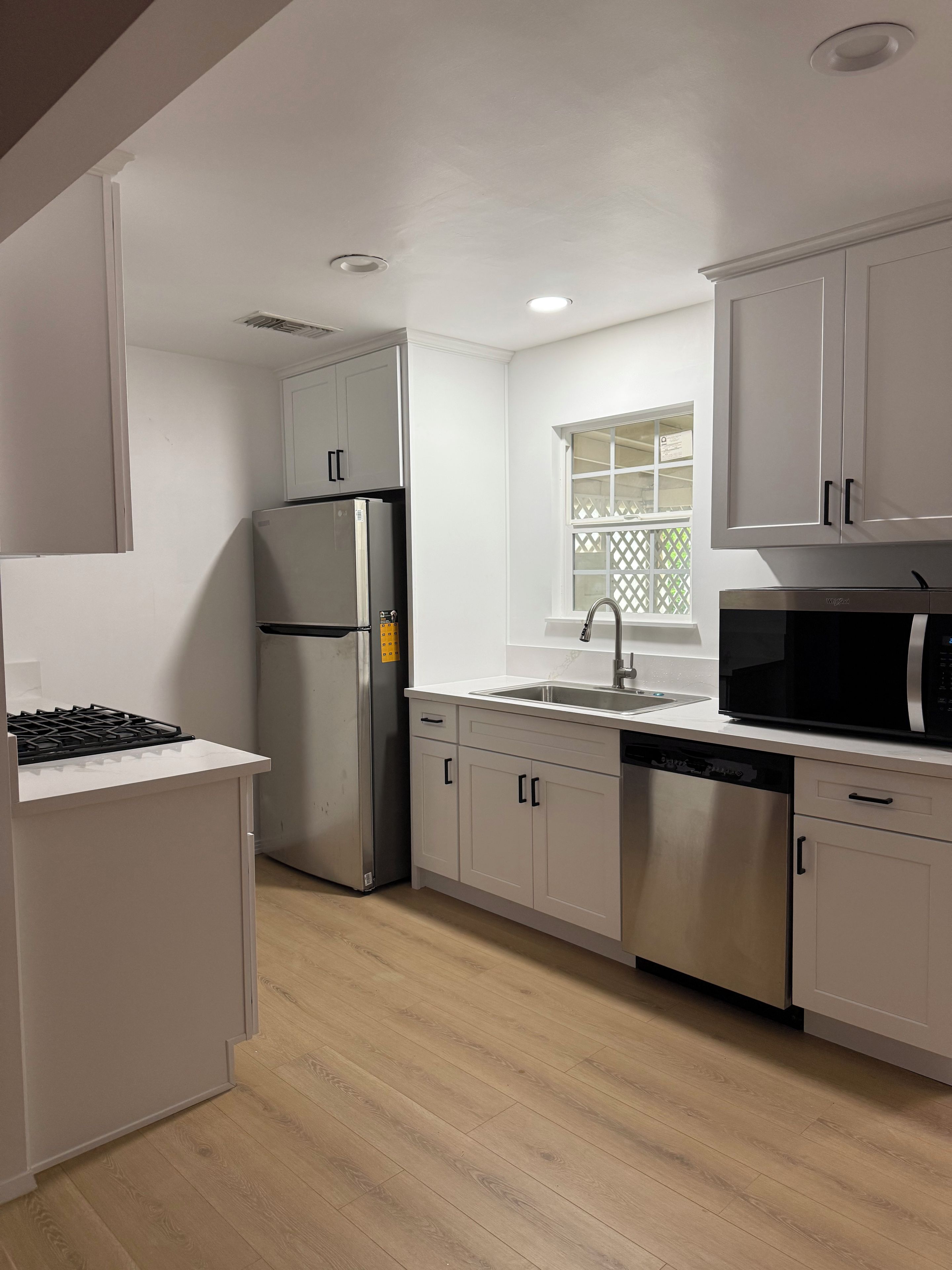 Una cocina moderna con armarios blancos, electrodomésticos de acero inoxidable y piso de madera.