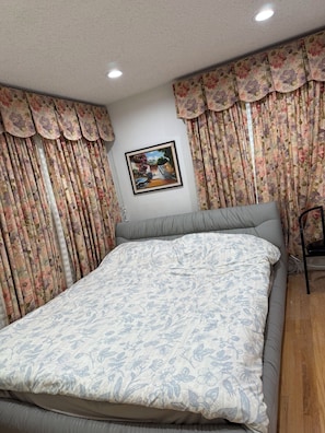 Ein Schlafzimmer mit einem Bett, floralen Vorhängen, einem gerahmten Bild an der Wand und einem Sessel.