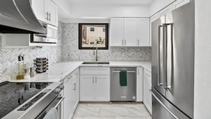 A modern kitchen with white cabinetry, a stainless steel refrigerator, a dishwasher, and a black induction cooktop. - DaZzling Waterfront 3-bedroom Pool/Hot tub/Gym in N. Padre Island (Corpus Christi)