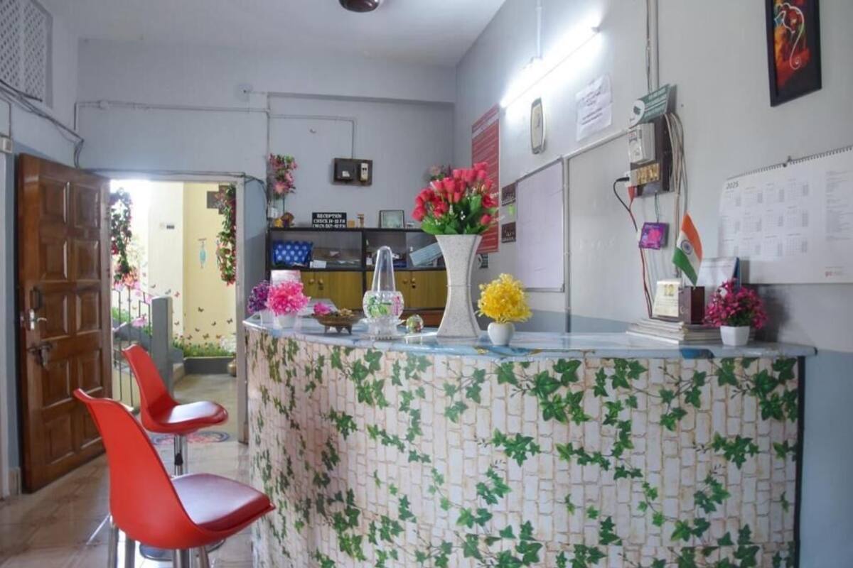 Uma área de recepção com balcão em azulejo, cadeiras vermelhas e diversos objetos decorativos, incluindo flores e um calendário.