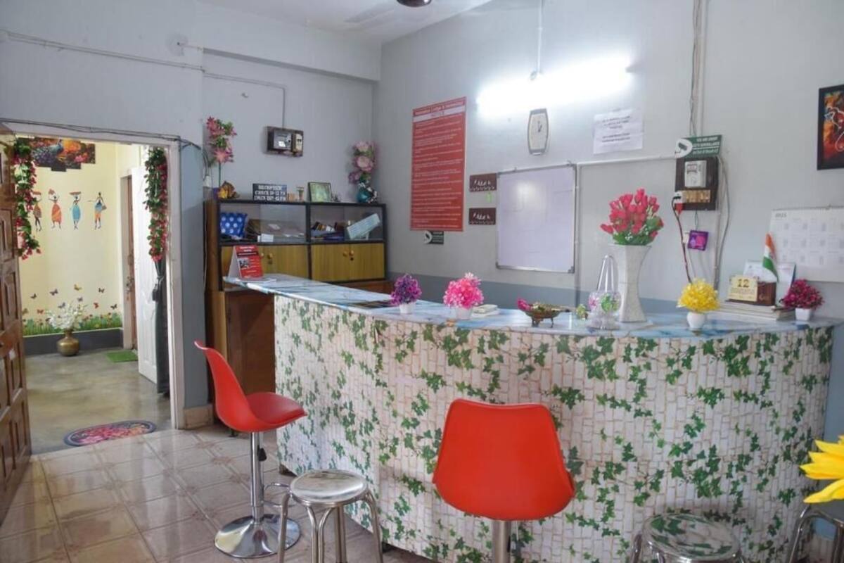 Uma área de recepção com balcão, cadeiras vermelhas, um quadro branco e um mural de avisos.