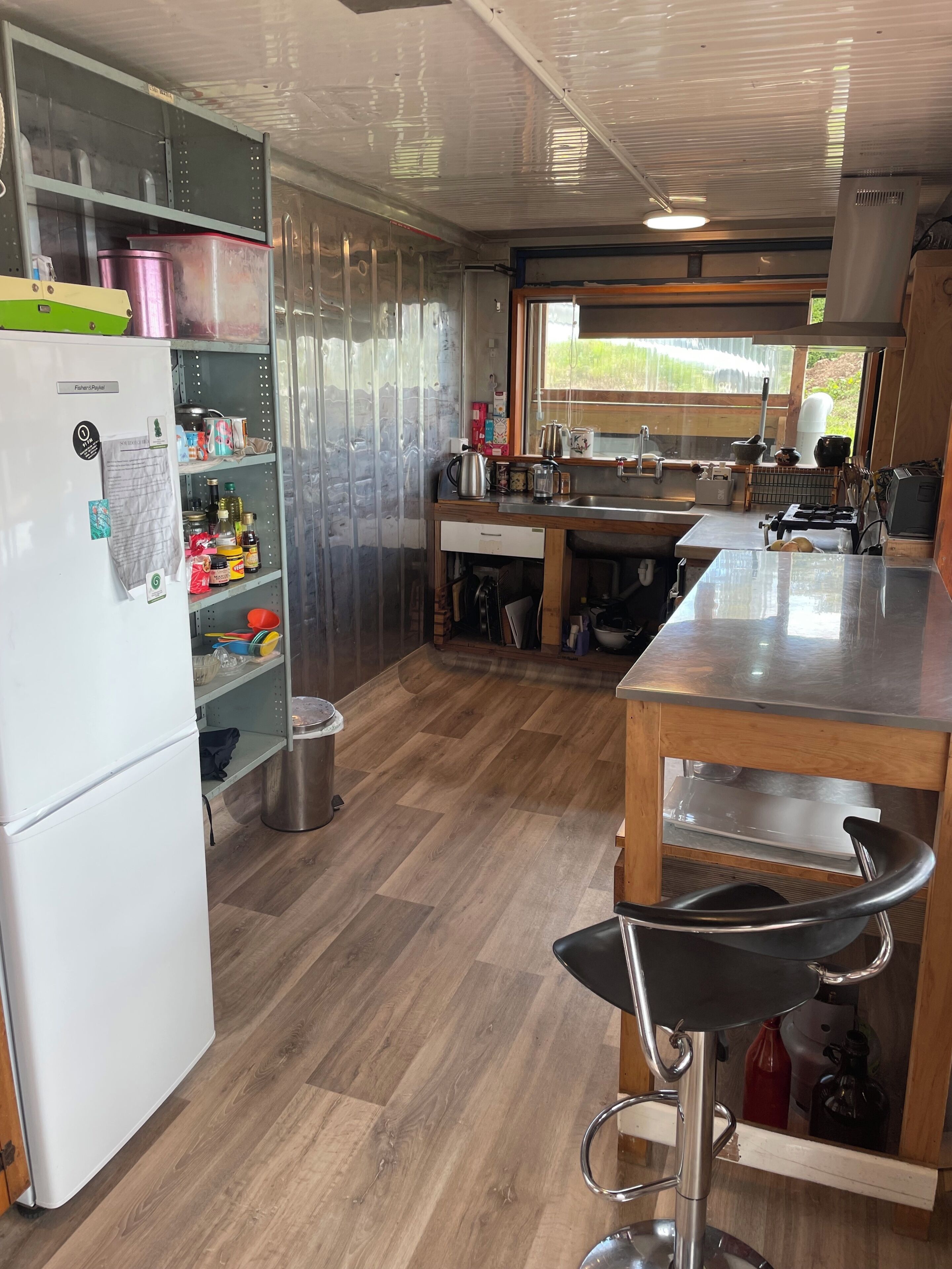A kitchen with a refrigerator, shelves, a sink, and a window.