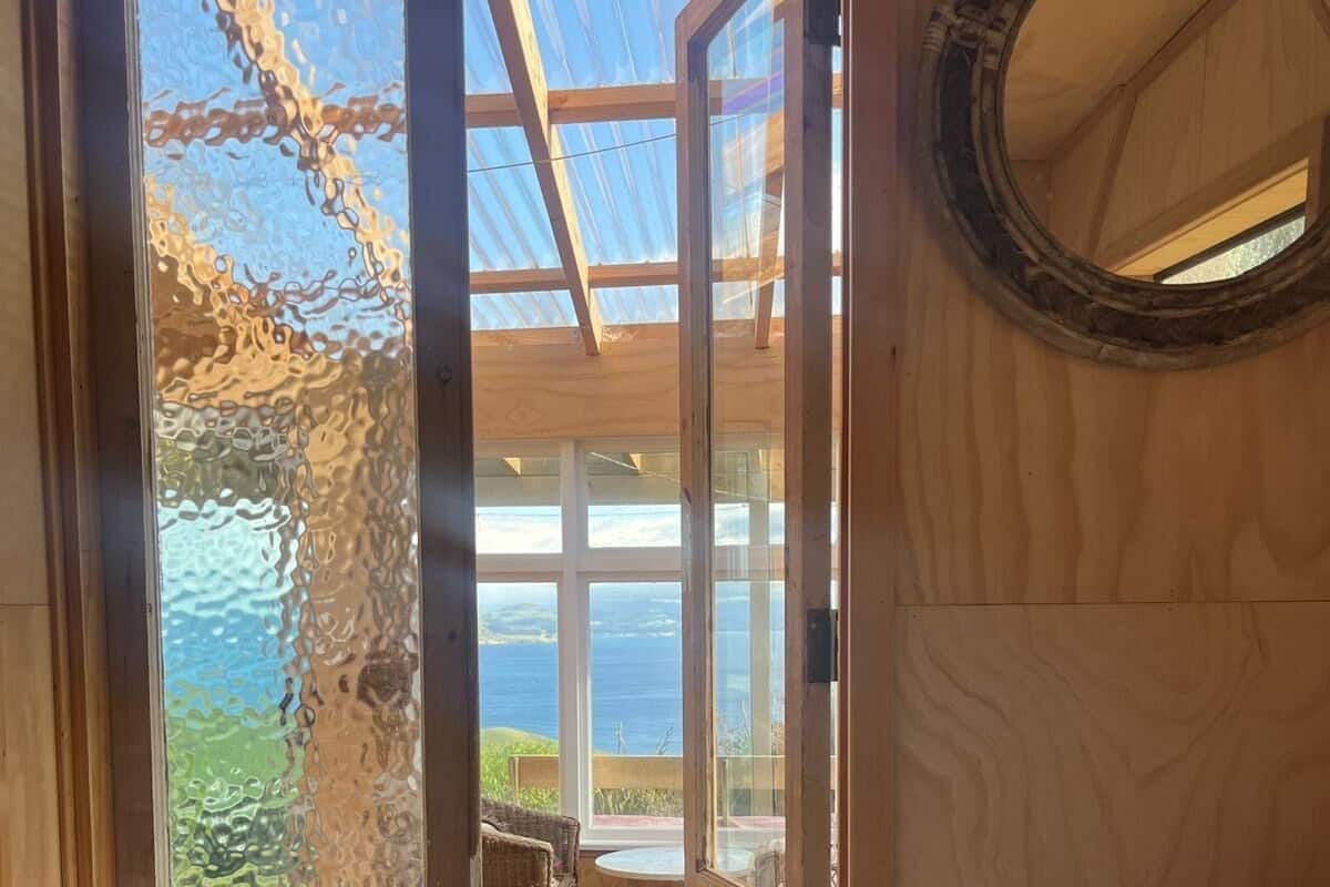 Ein Holzinnenraum mit einer großen Glastür, die auf einen Balkon mit Meerblick führt.