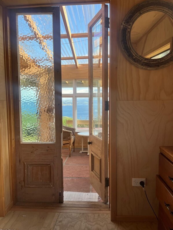 En interiör med träinredning och en stor glasdörr som leder ut till en balkong med utsikt över havet.