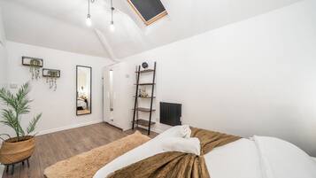 Ein modernes Schlafzimmer mit Bett, Nachttisch, Spiegel, Heizkörper und einem Regal mit Dekoration.
