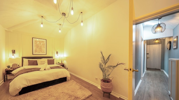 Un dormitorio con cama, lámparas de noche, un cuadro en la pared y una planta en maceta.