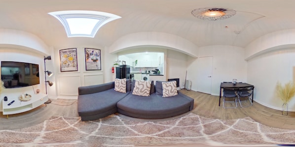 Una sala de estar moderna con un sofá curvo, un televisor de pantalla plana y una zona de comedor con una mesa pequeña y sillas.