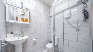 Un baño moderno con lavamanos, inodoro y zona de ducha blancos.