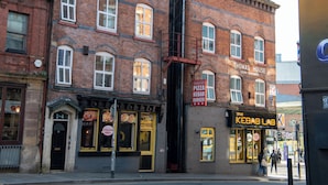 Un edificio de ladrillo con varias ventanas, un cartel que indica 'Thomas House', un edificio de apartamentos de lujo, y un restaurante 'Kebab Lab' con un menú visible.