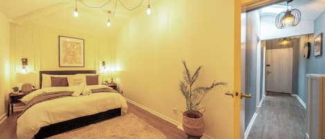 A bedroom with a bed, bedside lamps, a wall-mounted picture, and a potted plant.