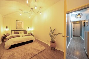 Une chambre à coucher avec un lit, des lampes de chevet, un tableau accroché au mur et une plante en pot.