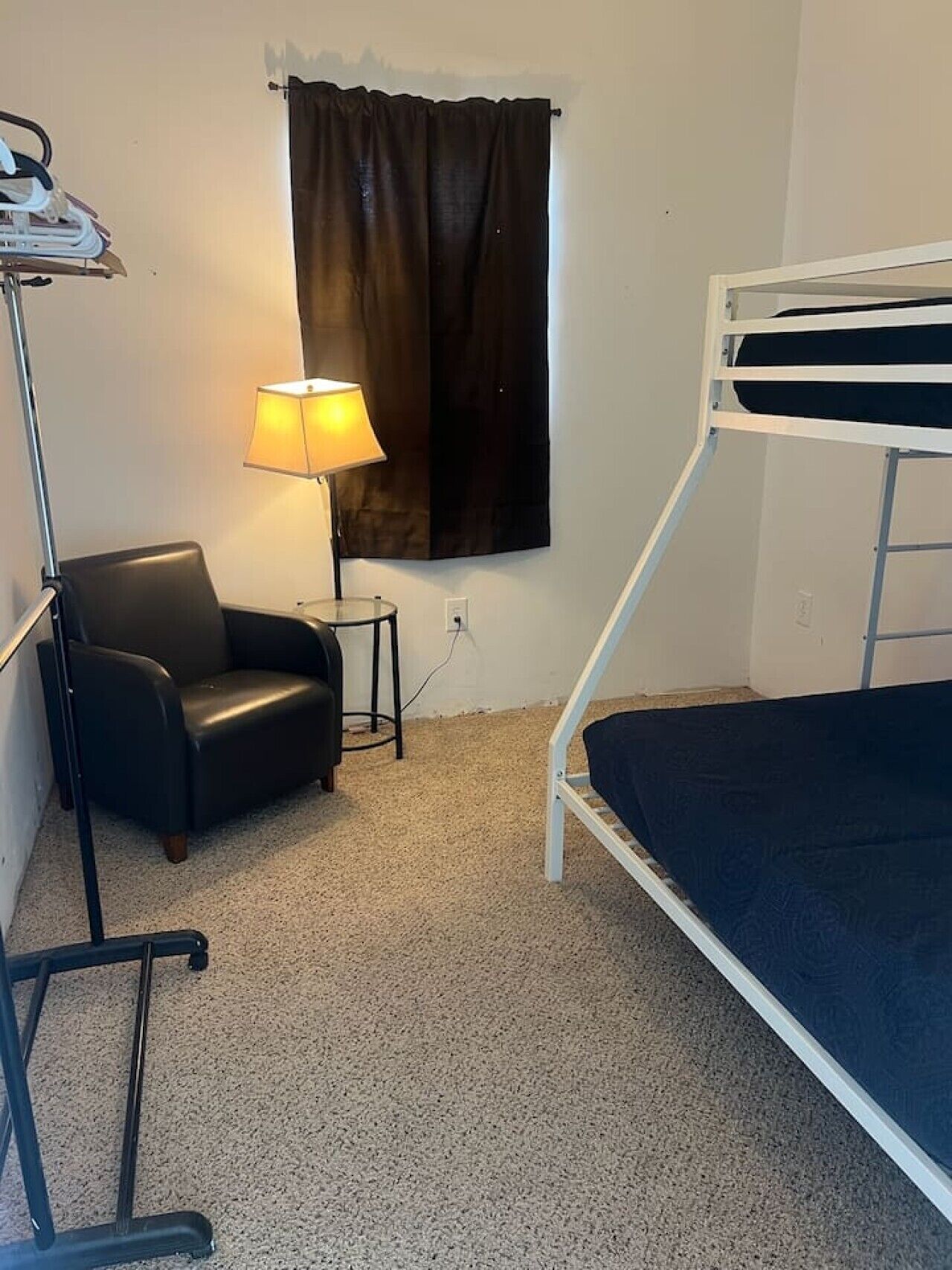 Una habitación con literas, una silla, una lámpara y un perchero.