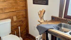 Un baño con paredes de madera, un inodoro blanco, un lavabo con encimera de madera y un cuadro enmarcado de una persona escalando una montaña.