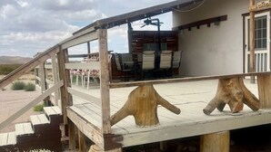 Una terraza de madera con zona de comedor, escalera y un edificio de fachada blanca.
