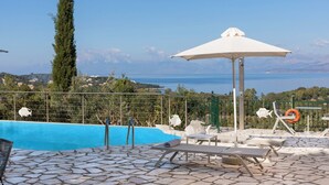 A pool area with lounge chairs, a lifebuoy, and a view of the sea. - Villa Melioris, Divine Sea Views, Private Pool, Spacious Furnished Terrace,. (Corfu)