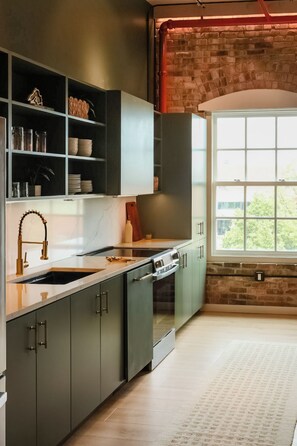 A modern kitchen with a marble countertop, stainless steel appliances, and a brick wall. - Aerial East | The Brix | Luxe Loft in Canal Park (Duluth)