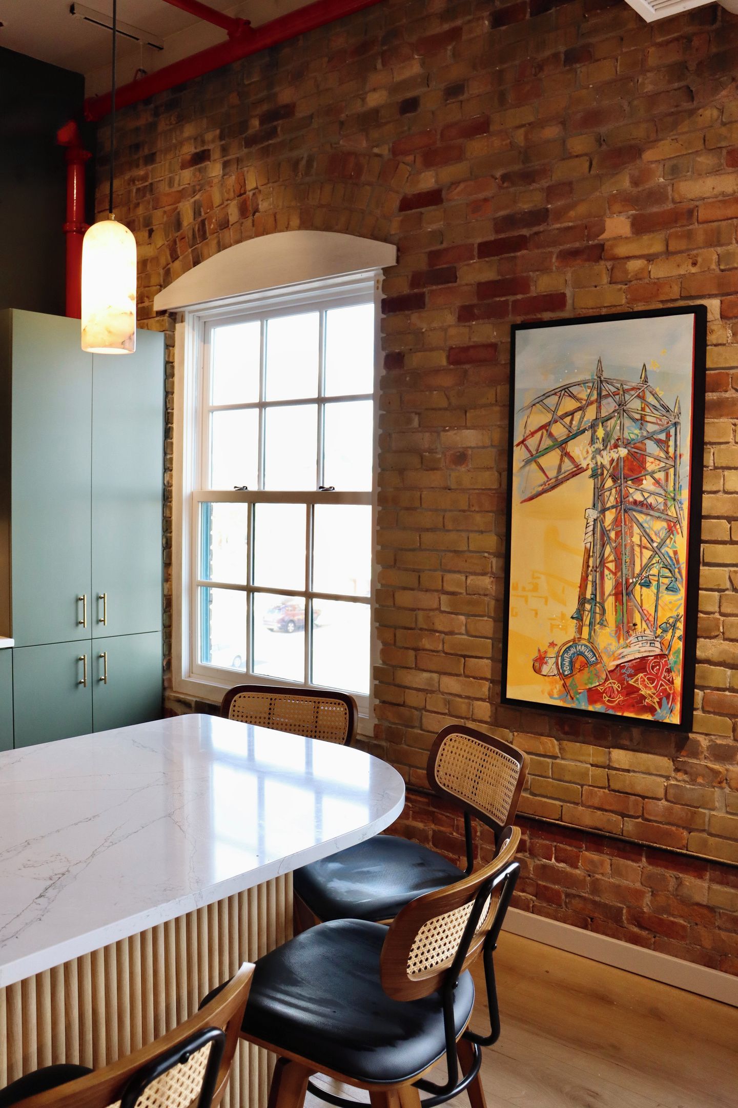 A dining area with a marble table, wooden chairs, a brick wall, and a large window.