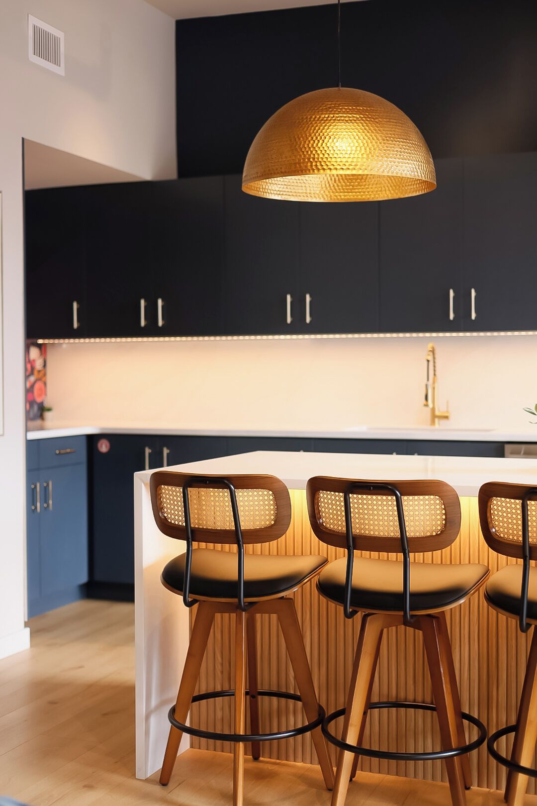 A modern kitchen with dark cabinets, a white countertop, and a central island with three bar stools.