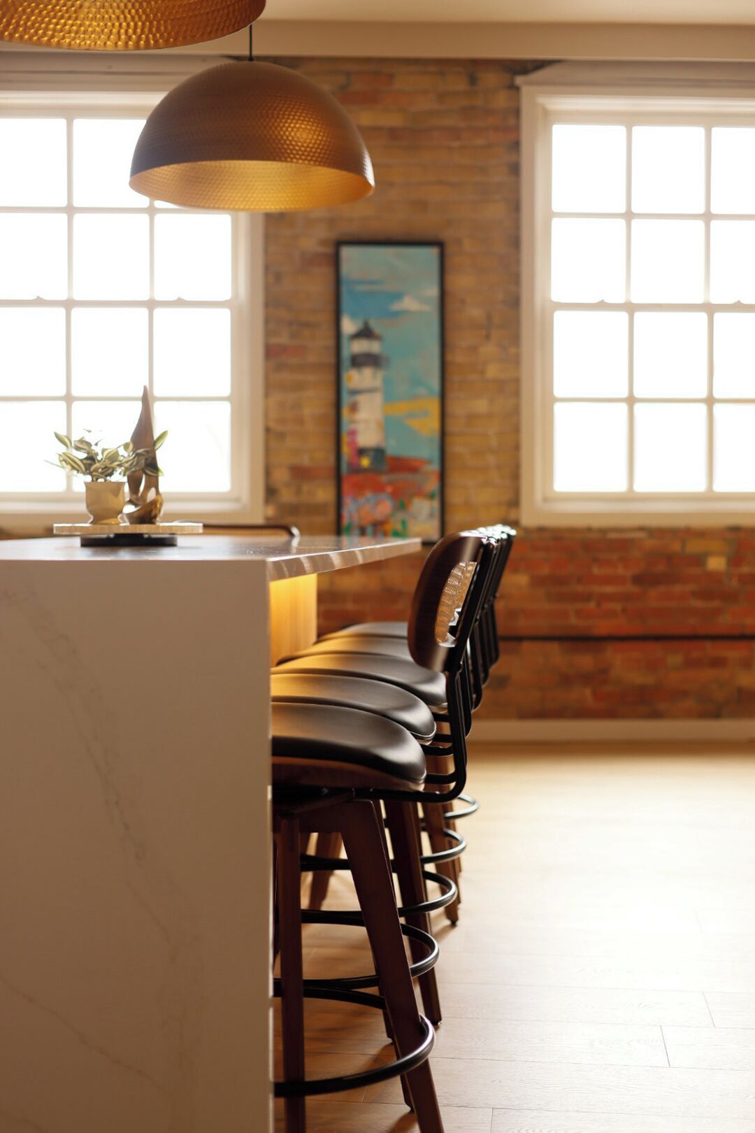 A bar area with a long counter, multiple bar stools, and a hanging pendant light.