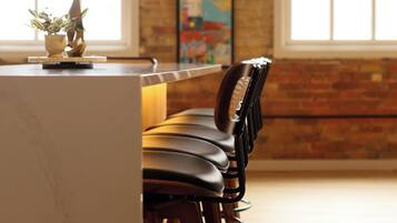 A bar area with a long counter, multiple bar stools, and a hanging pendant light.