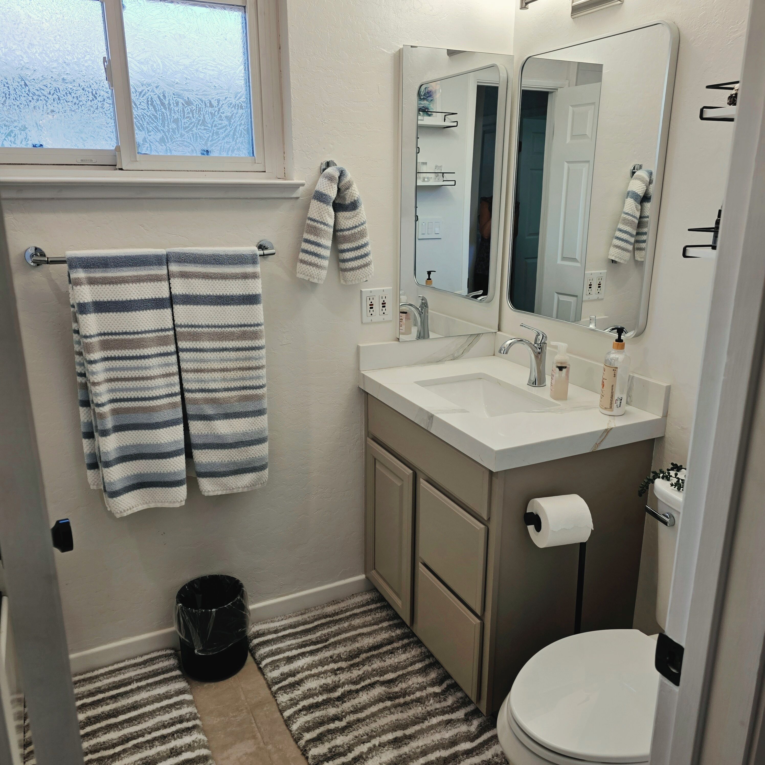 A bathroom with a window, a sink with a mirror, a toilet, and striped towels.