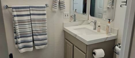 A bathroom with a window, a sink with a mirror, a toilet, and striped towels.