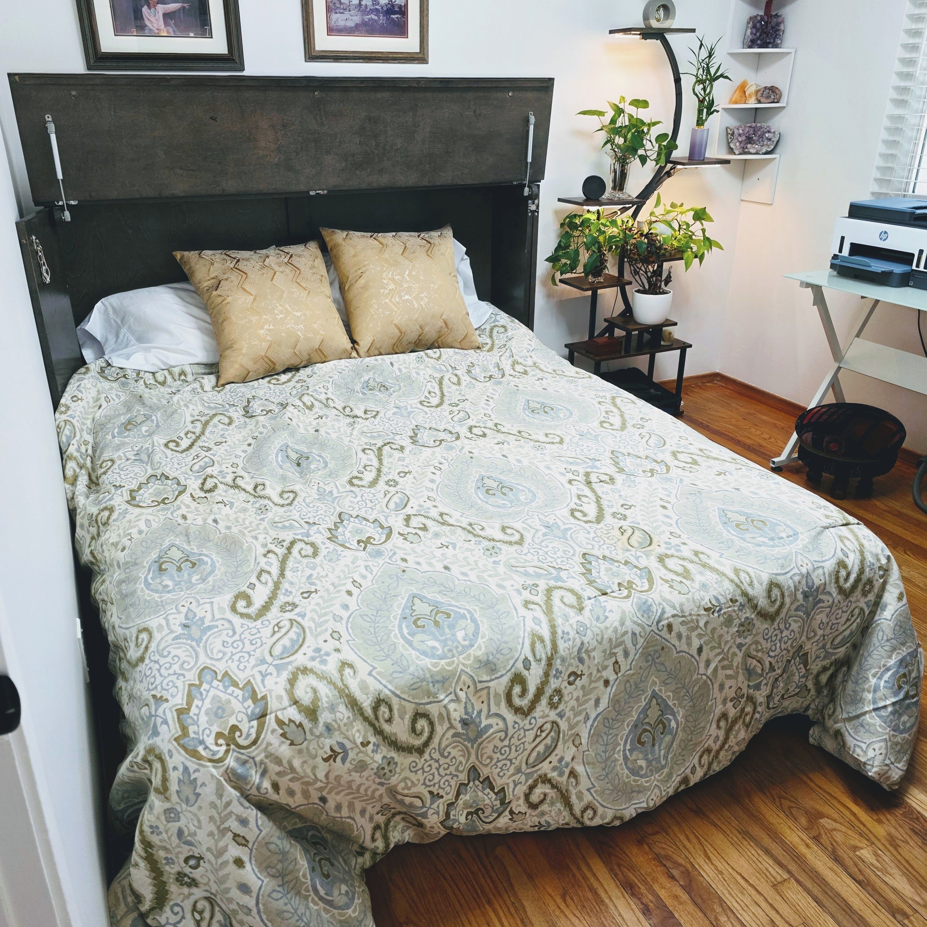 Una cama con ropa de cama estampada, un cabecero y una mesita de noche con una lámpara y una planta en maceta.