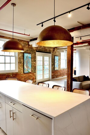 A modern kitchen with a large island, pendant lighting, and exposed brick walls. - Aerial Lofts | The Brix | Luxe Loft in Canal Park (Duluth)