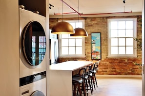 A kitchen with a large island, hanging pendant lights, and a brick wall. - Aerial Lofts | The Brix | Luxe Loft in Canal Park (Duluth)