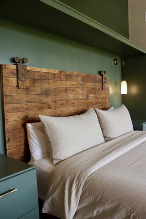 A bedroom with a wooden headboard, a bed with white bedding, and a nightstand with a drawer. - Aerial Lofts | The Brix | Luxe Loft in Canal Park (Duluth)