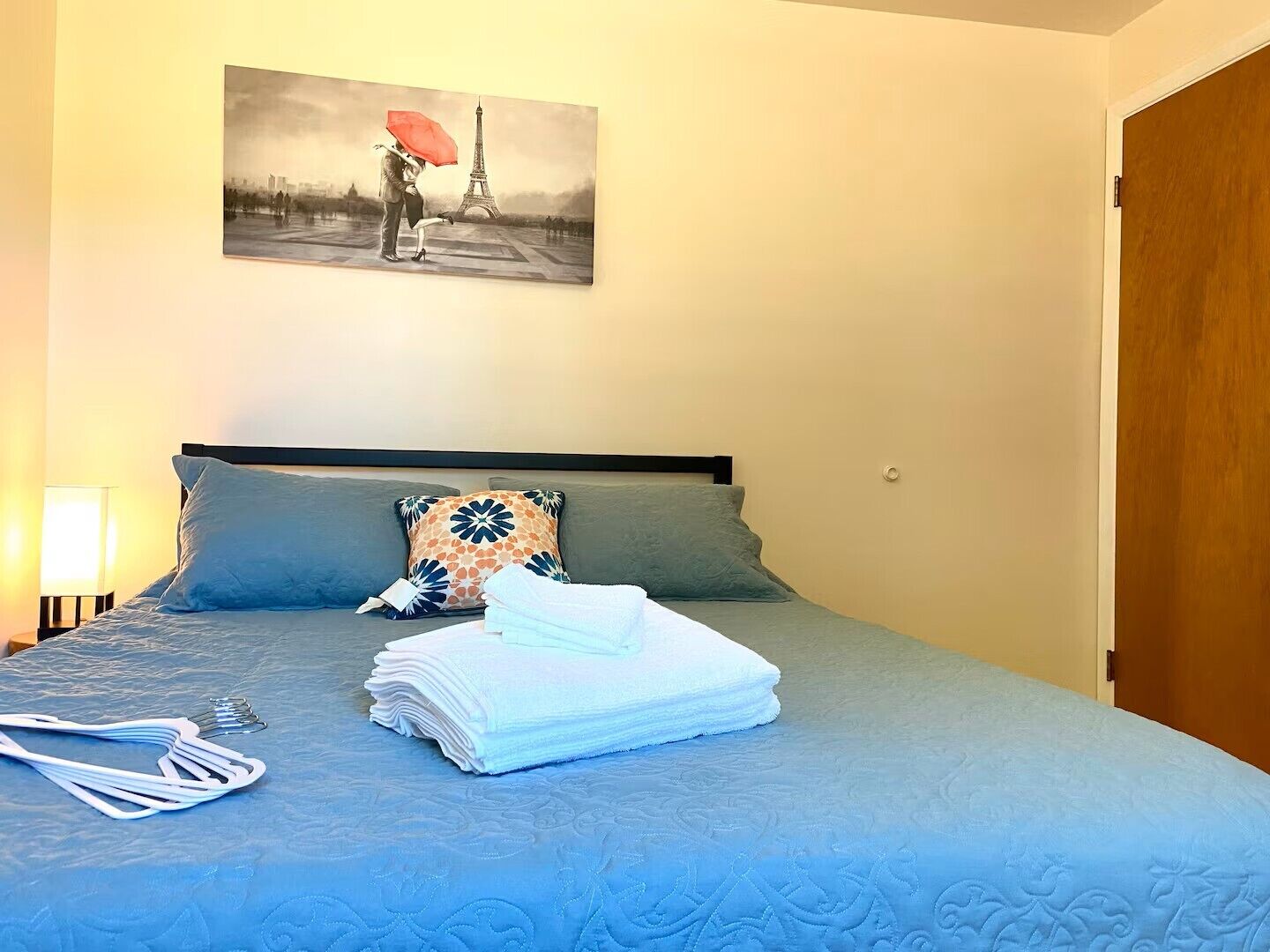 Ett hotellrum med en säng, en kudde, en hopvikt handduk och en tavla som föreställer Eiffeltornet.