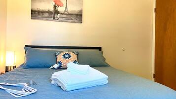 Ett hotellrum med en säng, en kudde, en hopvikt handduk och en tavla som föreställer Eiffeltornet.
