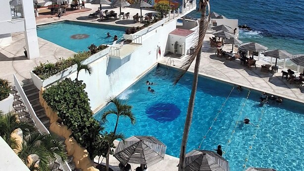 Ein Pool in einem Resort mit freiem Blick auf das Meer, Palmen und ein weißes Gebäude.