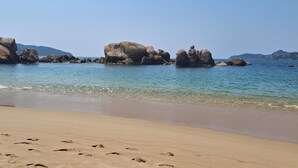 Ein Strand mit großen Felsen, klarem Wasser und Fußabdrücken im Sand.