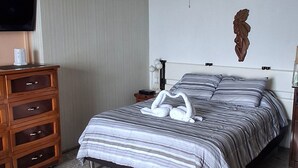 Ein Schlafzimmer mit Bett, Holzkommode, Fernseher, Deckenventilator und einer Wanddekoration.