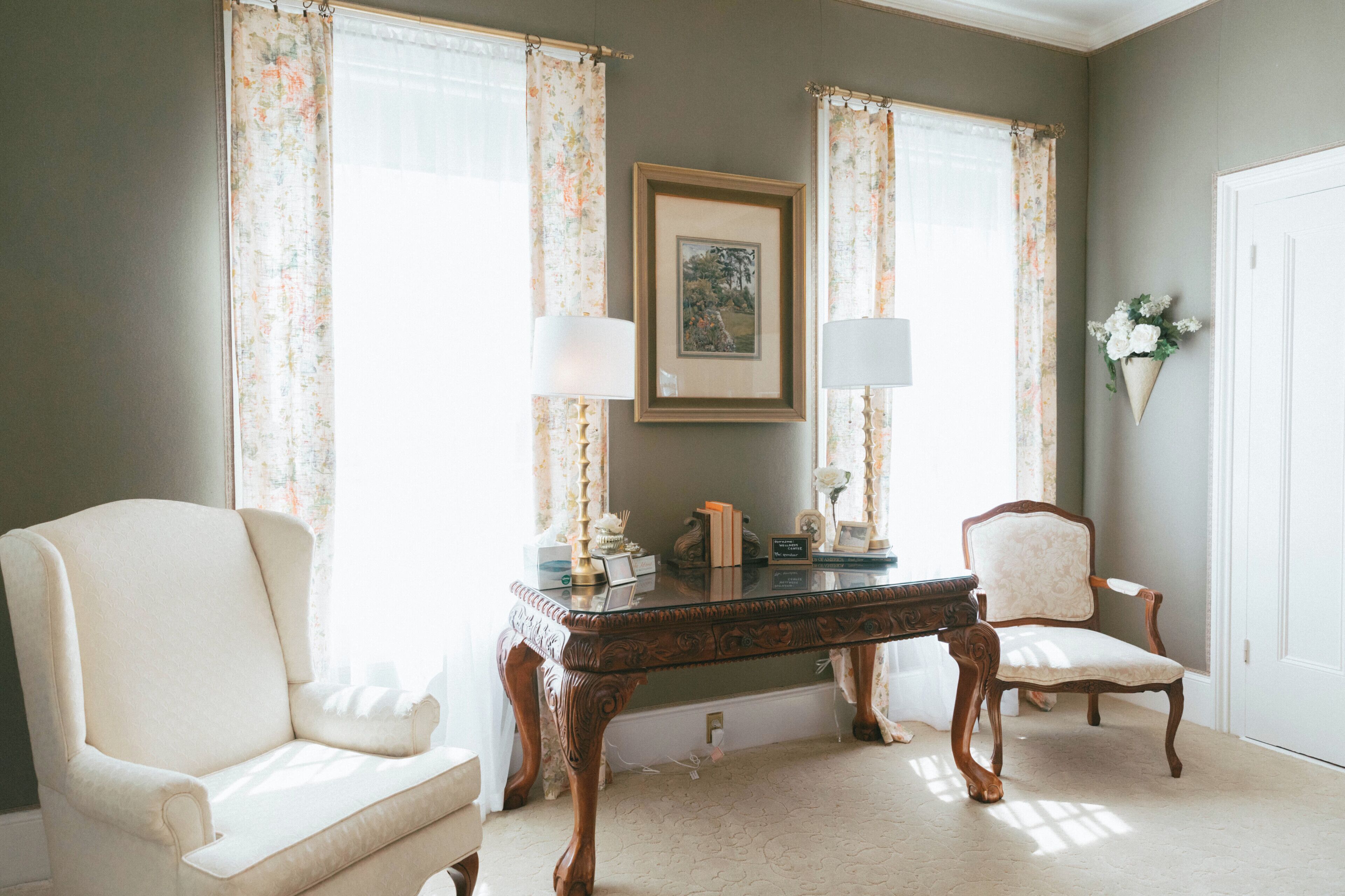 A room with a large window, a framed picture on the wall, a table, and two chairs.