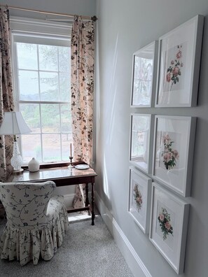 A room with a large window, a desk with a lamp, a chair, and multiple framed floral pictures on the wall. - The Bybee Estate (Central Point)