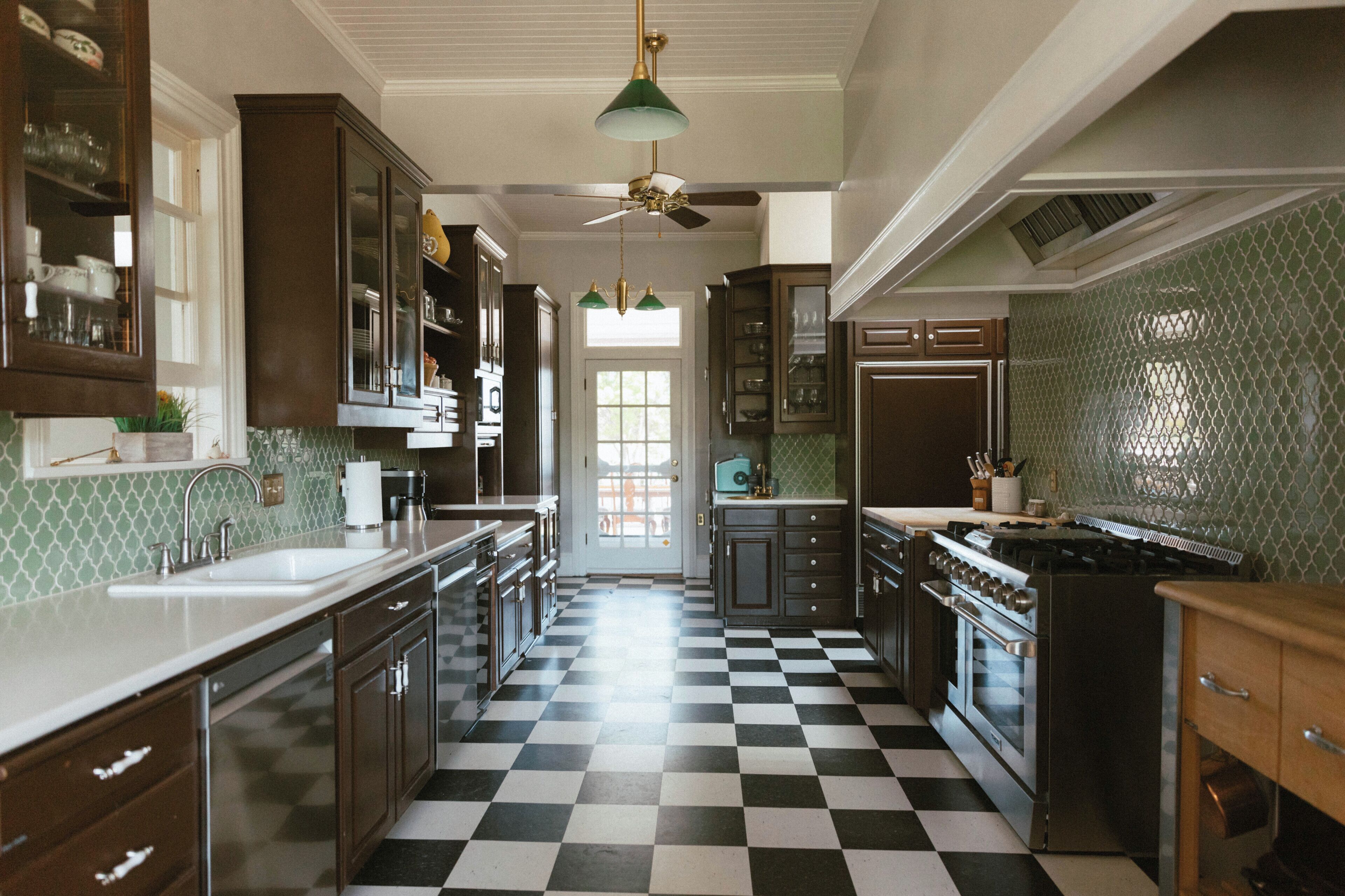 A kitchen with checkered flooring, dark wooden cabinets, a stove, and a ceiling fan.