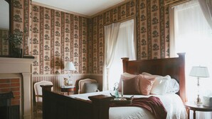 Un dormitorio tradicional con cama con dosel, chimenea y ventana con cortinas.