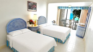 A hotel room with two beds, a small table with a lamp, a framed picture on the wall, and a view of the sea through a window. - Sunny Beach Inn (Ocho Rios)