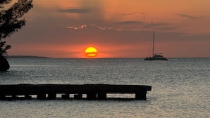 A sunset over a calm sea with a pier extending into the water. - Sunny Beach Inn (Ocho Rios)